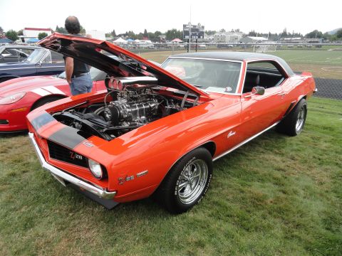 1964 Ford Fairlane - A highly modified 1969 Chevrolet Camaro Z28 is displayed with its hood open, revealing a prominent supercharger.