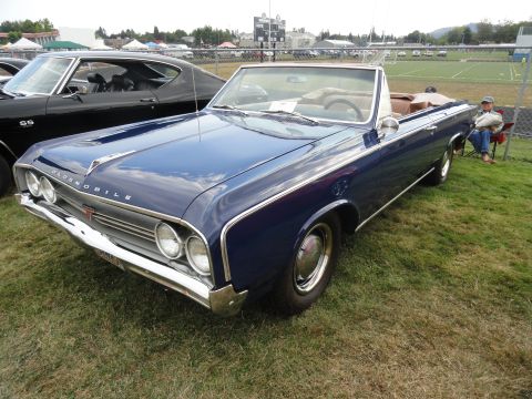1964 Ford Fairlane - A blue 1964 Oldsmobile convertible is parked on grass at a car show, with another car visible to the left.