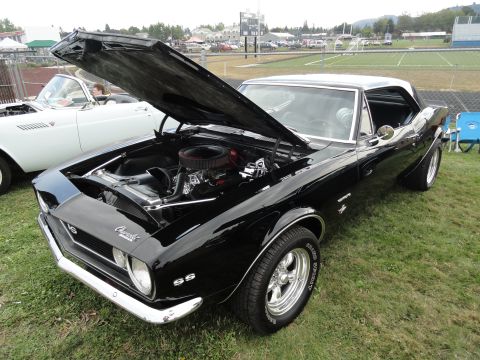 1964 Ford Fairlane - A black 1967 Chevrolet Camaro SS is displayed with its hood open, parked on a grassy field at a car show.