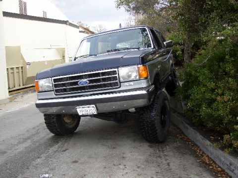 1989 Ford Bronco - This 1989 Ford Bronco features a prominent chrome grille and 4x4 badging, with its front tires angled towards the curb.