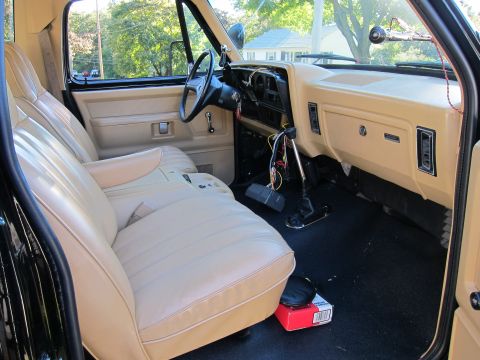 1987 Dodge 1500 - The interior of a pickup truck shows tan seats and dashboard with exposed wiring near the gear shifter.