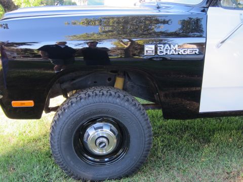 1987 Dodge 1500 - Close-up view of a black and white pickup truck's fender, the 'Ram Charger' badging and a off-road tire.