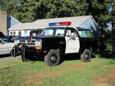 1987 Dodge 1500 - This two-tone police SUV is parked on a grassy lawn in front of a residential building.