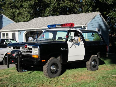 1987 Dodge 1500 - A black and white police SUV with a light bar is parked on a grassy lawn in front of a residential building.