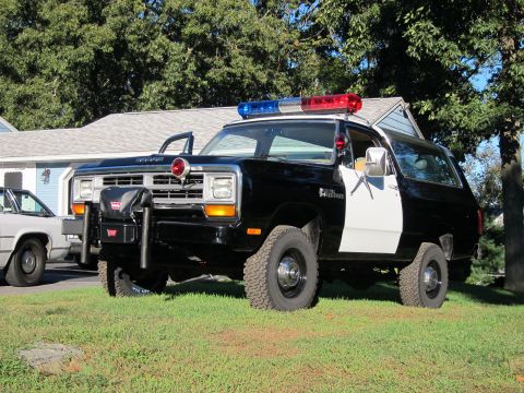 1987 Dodge 1500 - This 1987 Dodge 1500 police SUV is parked on a grassy lawn with a house and trees in the background.