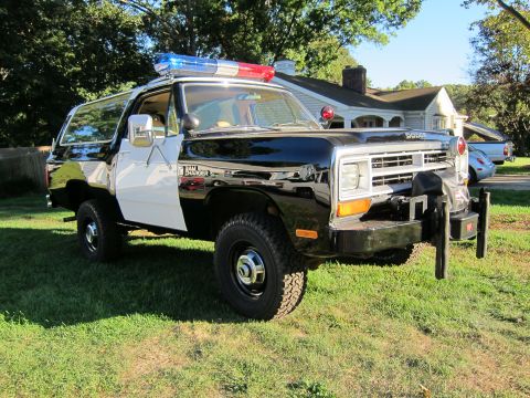 1987 Dodge 1500 - This 1987 Dodge Ramcharger police SUV features a light bar and push bumper, parked on a grassy lawn.