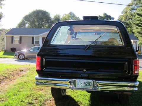 1987 Dodge 1500 - A black SUV is parked in a grassy yard with a house and a silver sedan in the background.