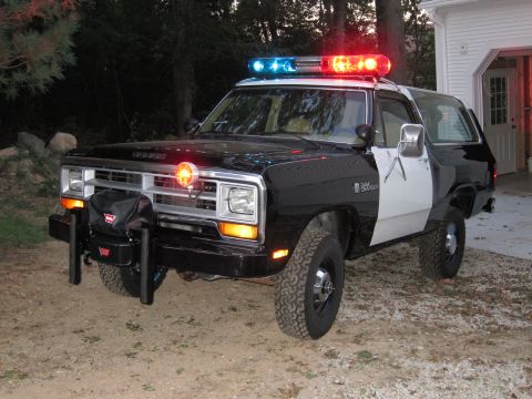 1987 Dodge 1500 - This police SUV, likely from the 1980s, is parked in a driveway with trees and a house in the background.
