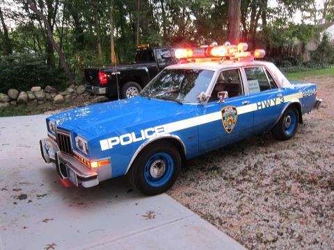 1987 Dodge 1500 - This police car has "POLICE" and "HWY 3" markings and is parked next to a black pickup truck.