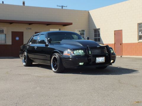 2003 Ford Crown Victoria - Blacked-out Crown Vic angled in a parking lot by a beige building with red trim.