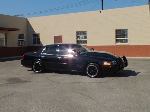 2003 Ford Crown Victoria - Profile of a murdered-out Crown Vic, sunlight flaring off the hood by a warehouse.