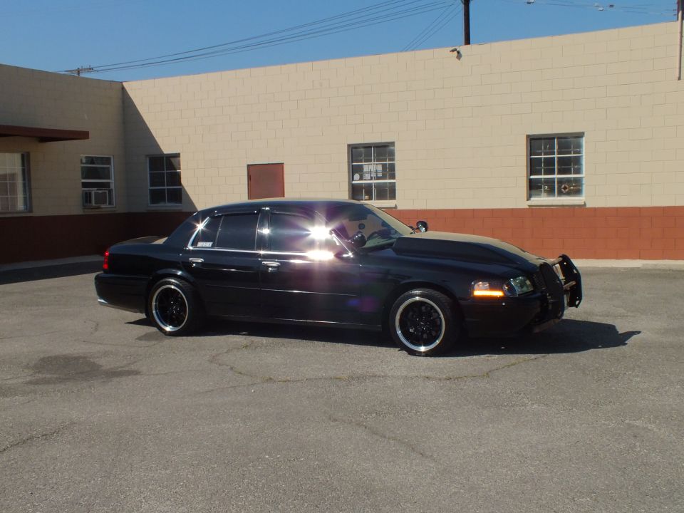 Black Ford Crown Victoria side profile with sun glare on hood in industrial lot