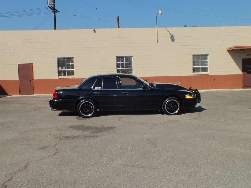 Black Ford Crown Victoria driver-side profile in lot beside windowed building