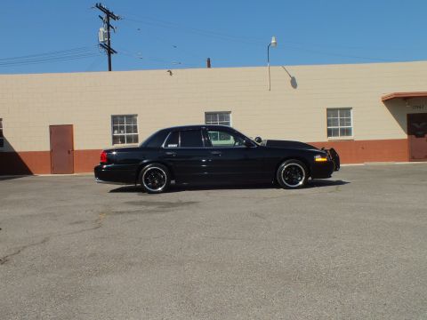 2003 Ford Crown Victoria - Crown Vic in profile beside a tan building, push bar visible at the front.