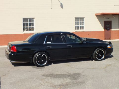 2003 Ford Crown Victoria - Rear-quarter view of a lowered Crown Vic by a beige building with red door trim.