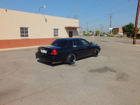 2003 Ford Crown Victoria - Rear-quarter of a blacked-out Crown Vic parked across a wide industrial lot.