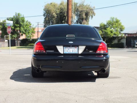 2003 Ford Crown Victoria - Tail-on shot showing the dual exhaust, SVT badging and a personalized EVIL VIC plate on a black sedan.
