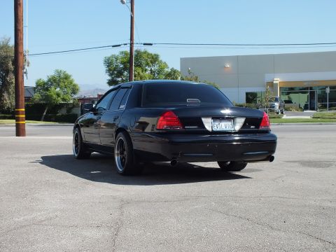 2003 Ford Crown Victoria - Driver-side rear angle of a black Crown Victoria, dropped low with EVIL VIC tag near an industrial building.