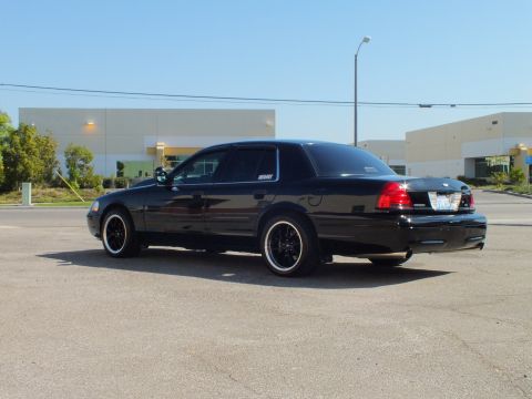 2003 Ford Crown Victoria - Low driver-side rear shot of a black Crown Victoria with deep-dish black wheels in front of warehouses.