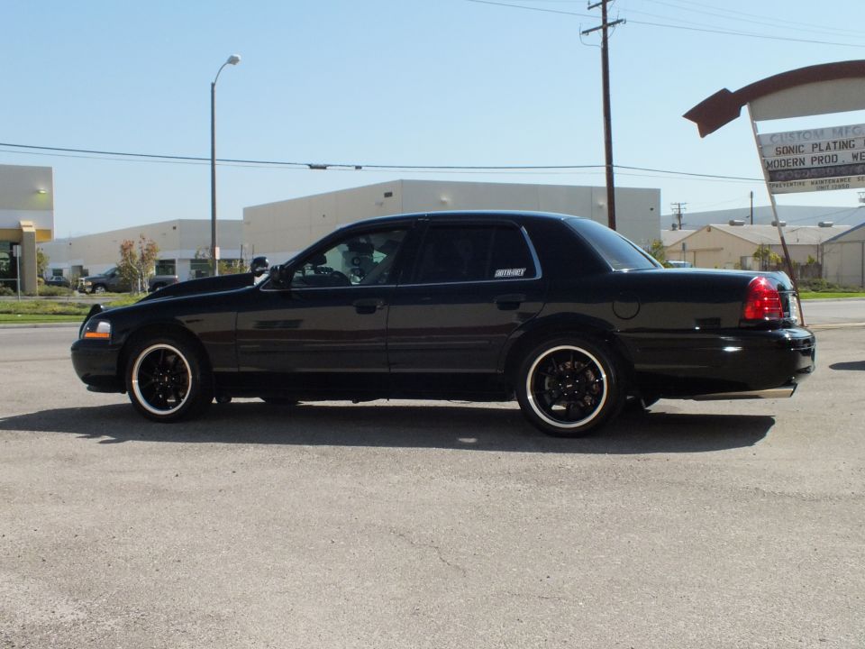 Black Ford Crown Victoria driver-side profile, lowered on black wheels near plating shop