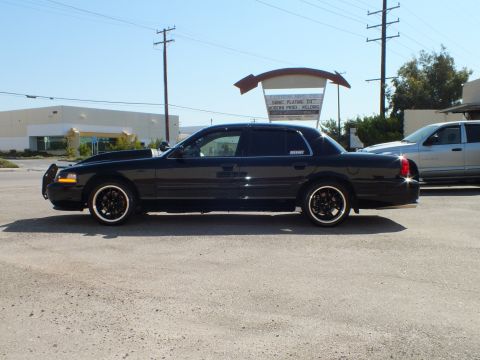 2003 Ford Crown Victoria - Side view of a black Crown Victoria fitted with a front grille guard, sitting low in an industrial yard.