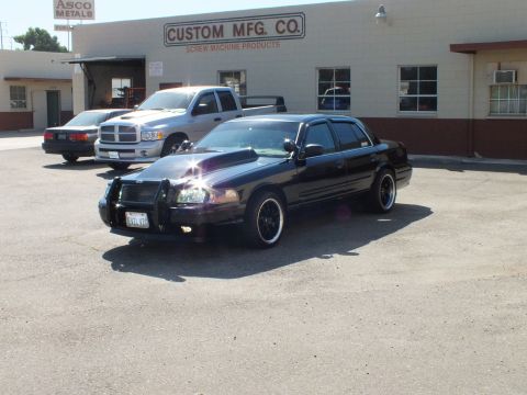 2003 Ford Crown Victoria - Front-quarter view of a push-bar Crown Victoria parked next to a silver Dodge Ram outside a shop.