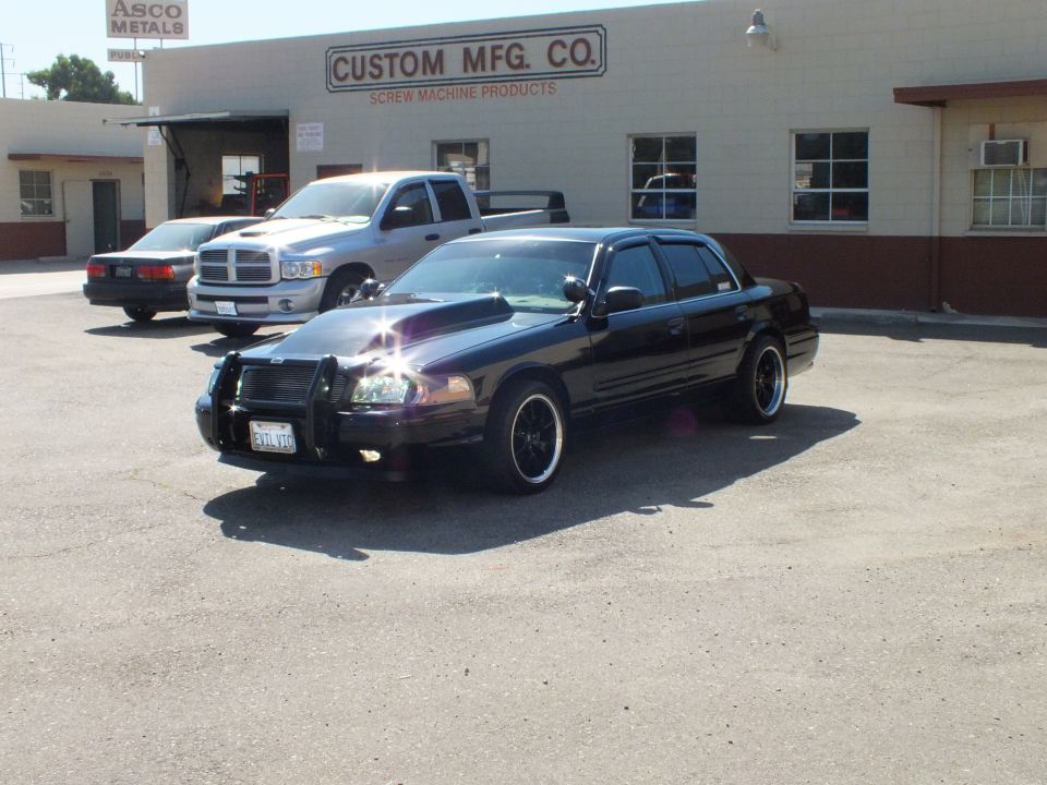Black Crown Victoria with push bar and amber lights beside Dodge Ram at Custom Mfg Co