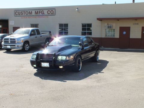 2003 Ford Crown Victoria - Sun-flare front shot of a black Crown Victoria with push bar and fog lamps next to a pickup.