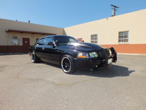 2003 Ford Crown Victoria - Glossy black Crown Victoria with grille guard shown from the front passenger side under blue sky.