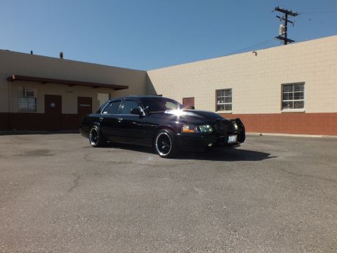 2003 Ford Crown Victoria - Distant front-quarter view of a black push-bar Crown Victoria in a large paved lot.
