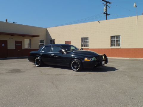 2003 Ford Crown Victoria - Black Crown Victoria with front guard photographed from the driver-front against a warehouse wall.