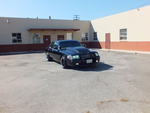 2003 Ford Crown Victoria - Black Crown Victoria with grille guard angled toward the camera in an industrial parking lot.
