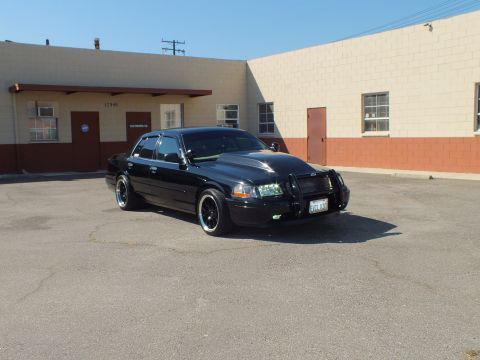 2003 Ford Crown Victoria - Passenger-front view of a black push-bar Crown Victoria with a California plate on dark wheels.