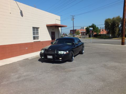 2003 Ford Crown Victoria - Black Crown Victoria with grille guard shot from the front corner beside a red-and-tan building.