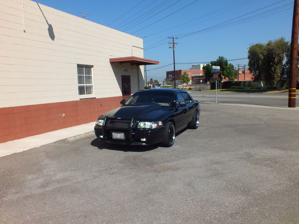 Black Crown Victoria front three-quarter with push bar parked against brick-trimmed wall