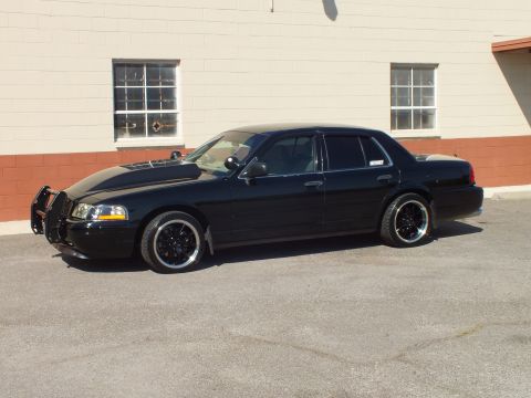 2003 Ford Crown Victoria - Side view of a blacked-out Crown Victoria sedan with grille guard, parked beside a brick building.