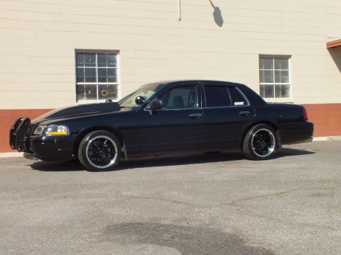2003 Ford Crown Victoria - Driver-side profile of a lowered black Ford sedan with grille guard and black multi-spoke wheels.