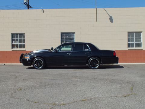 2003 Ford Crown Victoria - Full side profile of a glossy black Ford sedan with grille guard parked by a brick wall.