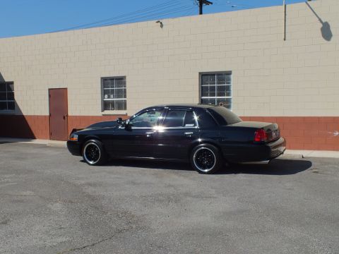 2003 Ford Crown Victoria - Rear three-quarter shot of a lowered black Ford sedan parked beside a warehouse.