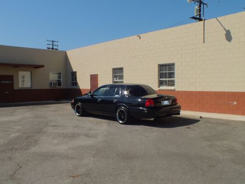 2003 Ford Crown Victoria - Rear three-quarter angle of a black Ford sedan with dual exhaust on cracked asphalt.
