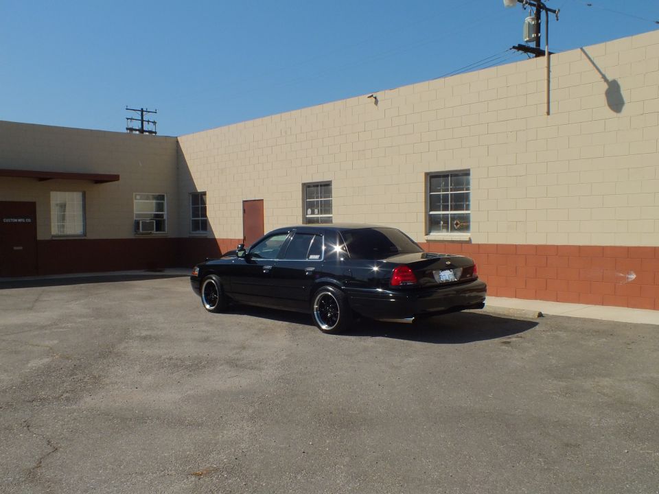 Black Crown Victoria rear quarter view parked in lot beside tan building
