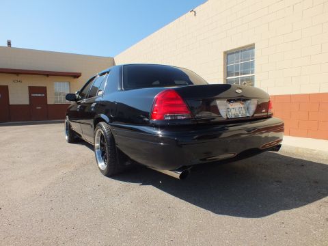 2003 Ford Crown Victoria - Low rear angle of a black Ford sedan with chrome exhaust tip on cracked asphalt.