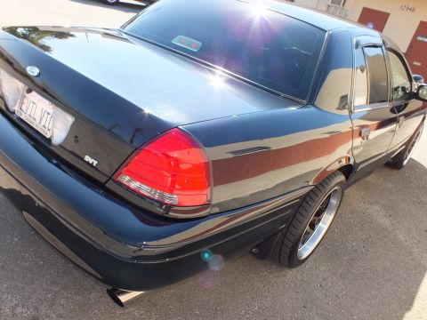 2003 Ford Crown Victoria - Angled rear quarter of a black Ford sedan with SVT badge and machined black wheel.