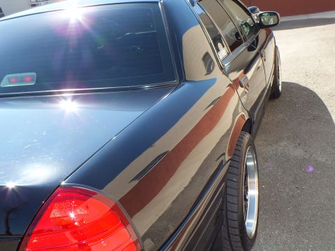 2003 Ford Crown Victoria - Tight detail of a black Ford sedan rear quarter showing taillight and machined wheel.