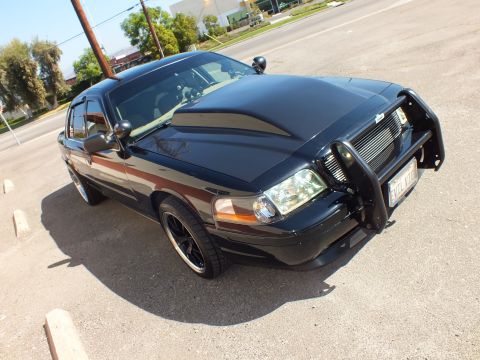 2003 Ford Crown Victoria - Front three-quarter of a black Ford sedan with grille guard, spotlight and visible plate.