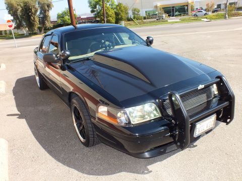 2003 Ford Crown Victoria - Front three-quarter of a blacked-out Crown Victoria with grille guard at a roadside lot.