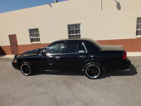 2003 Ford Crown Victoria - Passenger-side profile of a lowered black Panther-platform sedan with tinted windows and dark wheels