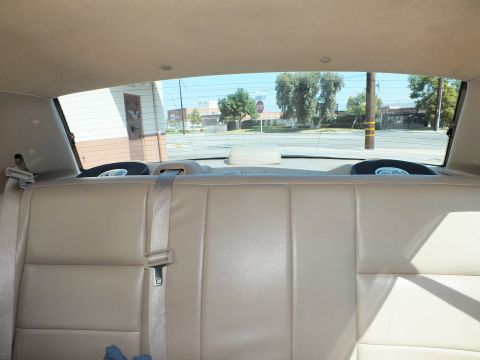 2003 Ford Crown Victoria - Rear bench seat of a sedan in tan upholstery with speakers mounted in the rear parcel shelf