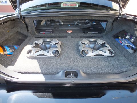 2003 Ford Crown Victoria - Centered trunk shot showing dual subwoofers below a row of amplifiers in a carpeted enclosure