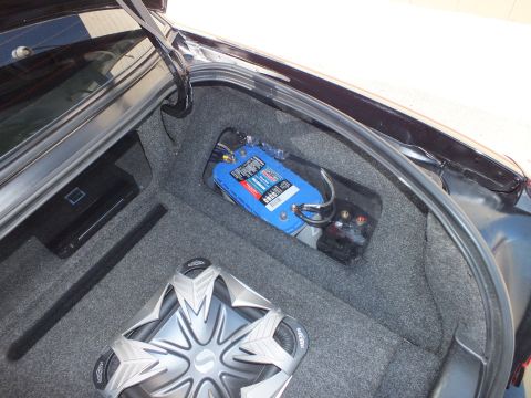 2003 Ford Crown Victoria - Trunk wiring view showing a blue distribution block with fuses beside a chrome subwoofer in carpet